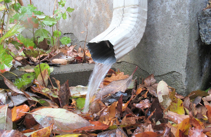 water flowing from a gutter into a downpipe clogged up with leaves