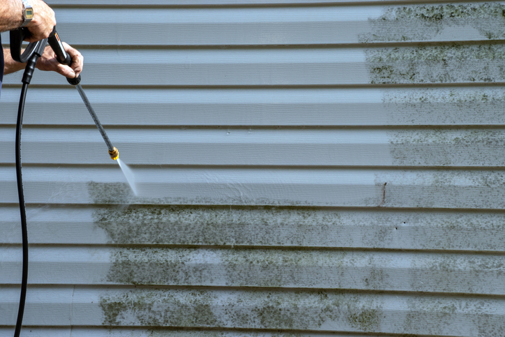 person power washing algae from the side of a building