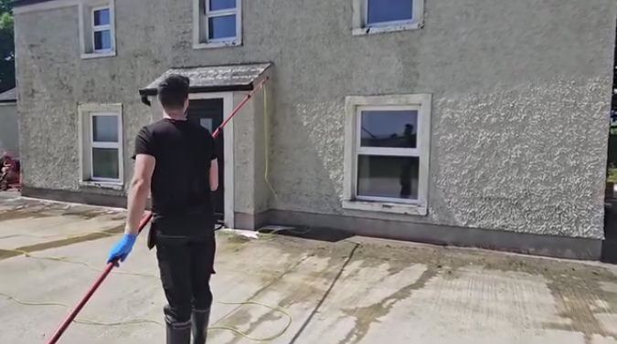 workers with a hose spraying a house to treat moss before soft washing