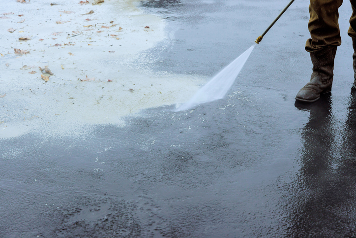 person power washing moss from a tarmac driveway